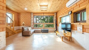 A cozy room with a wooden ceiling, a sofa, a TV, and large windows. - Tongyoung Blue House Spa Pension (Tongyeong)