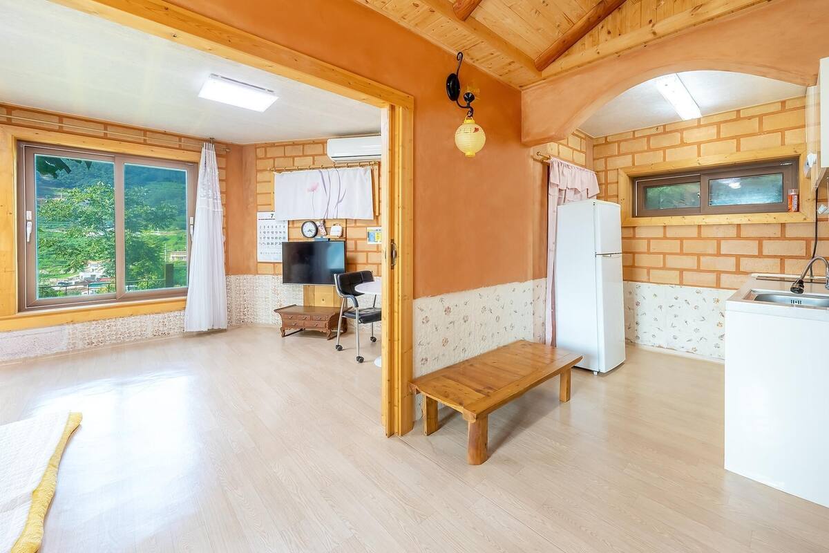 A compact kitchen with a wooden bench, a refrigerator, a sink, and a window overlooking greenery.
