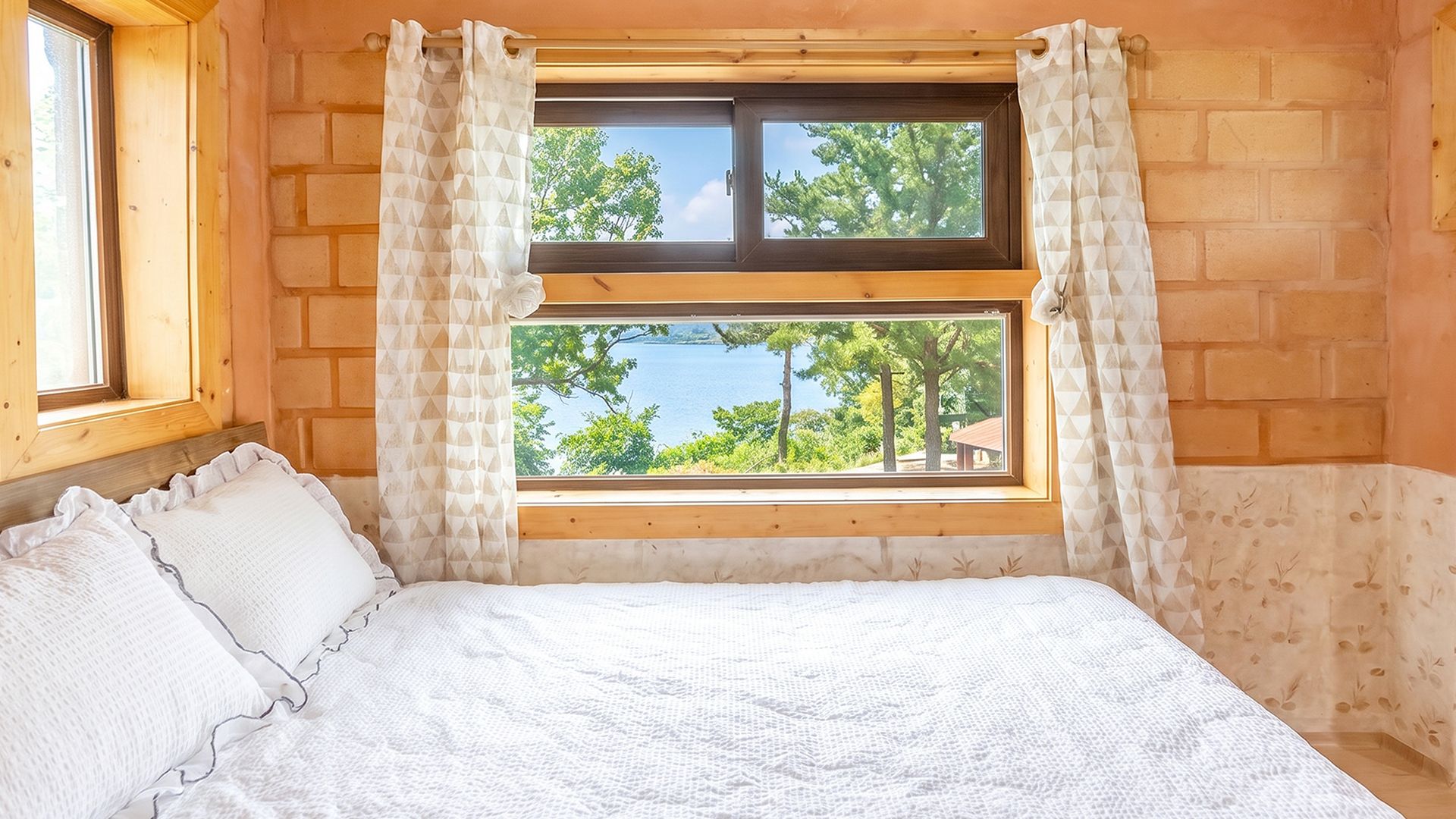 Un dormitorio con una cama, un ventanal con cortinas y vistas a árboles y agua.