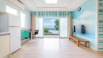 Una habitación con cocina, comedor con sillas, un banco, televisor montado en la pared y balcón con vistas.