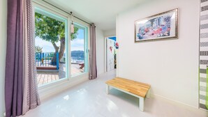 A hallway with a bench, a large window with curtains, a door, and a framed picture on the wall. - Tongyoung Blue House Spa Pension (Tongyeong)