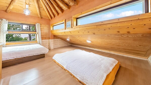 A cozy room with two beds, wooden ceiling beams, and large windows offering a view of the outdoors. - Tongyoung Blue House Spa Pension (Tongyeong)
