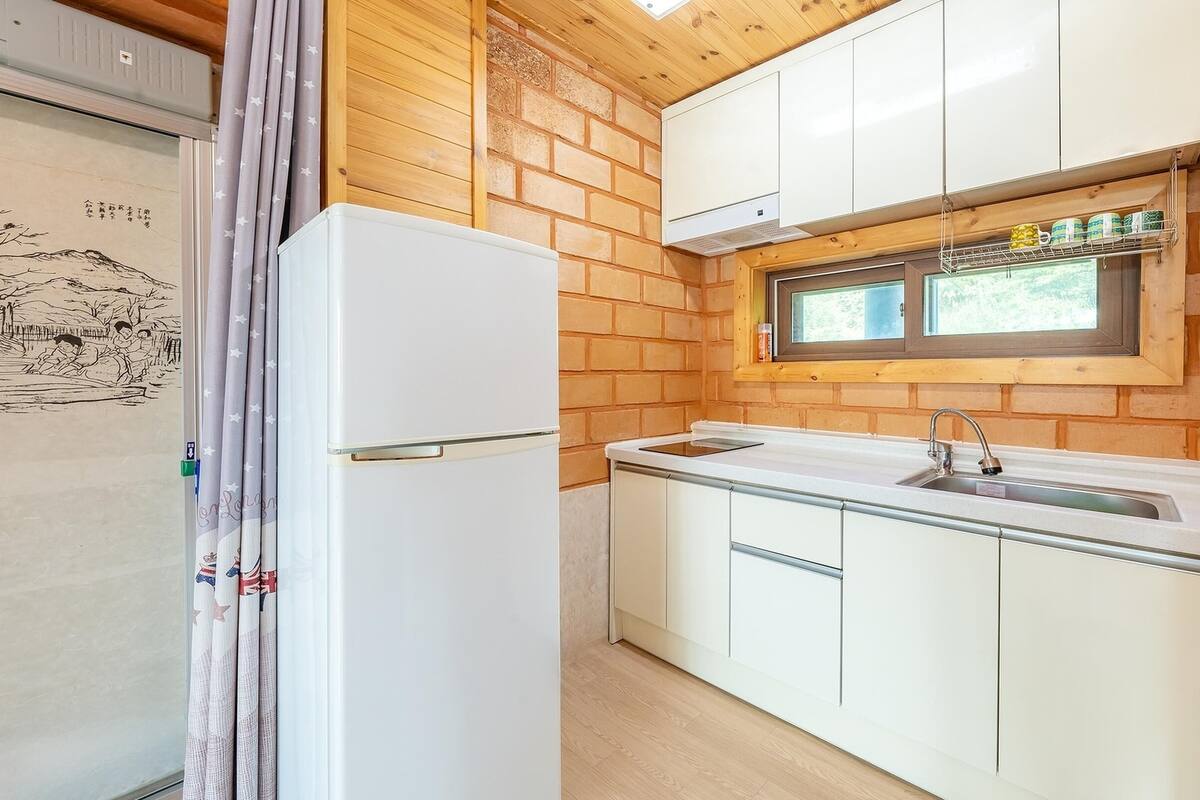 A compact kitchen with a built-in refrigerator, a window above the sink, and wooden walls.
