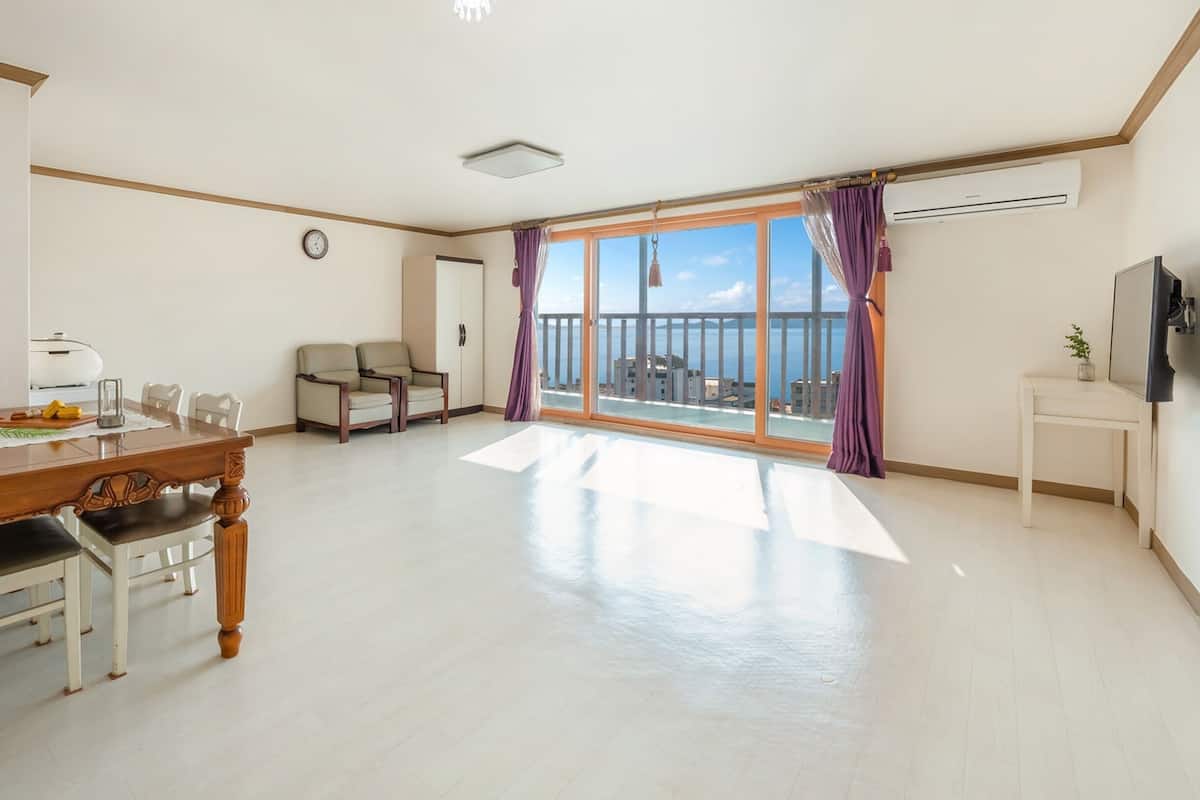 A spacious living area with a dining table, chairs, a sofa, a TV, and a balcony with a view.