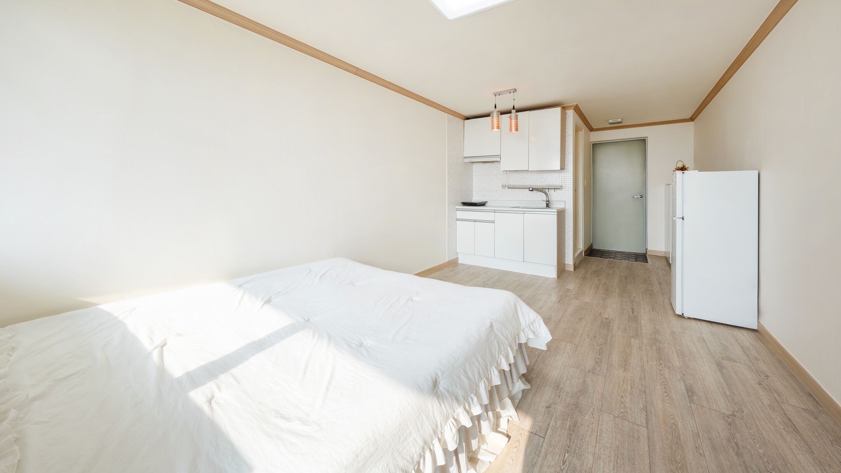 A bedroom with a large bed, a kitchenette, and a door leading to a bathroom.