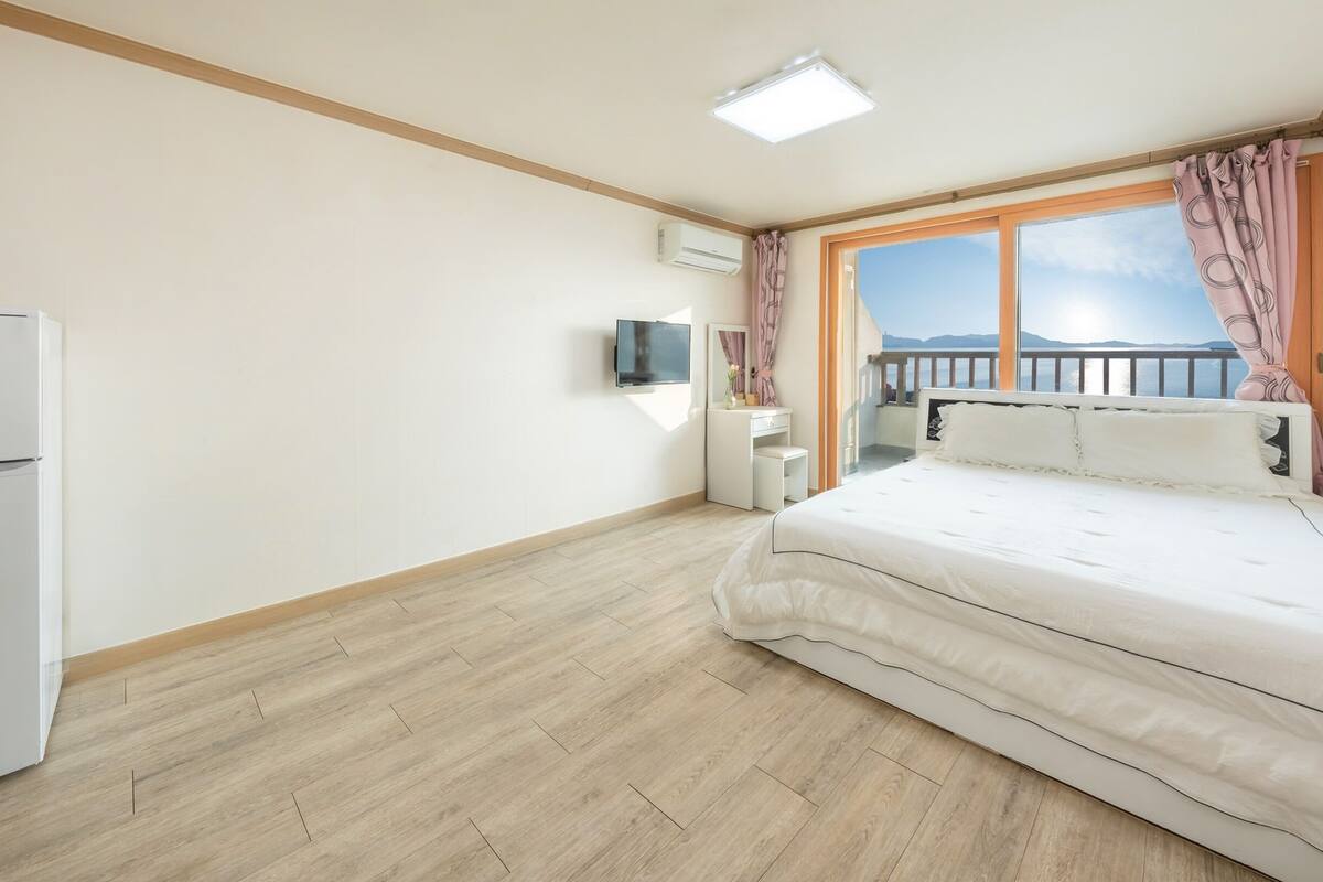 A bedroom with a bed, a desk, a television, and a window with curtains.