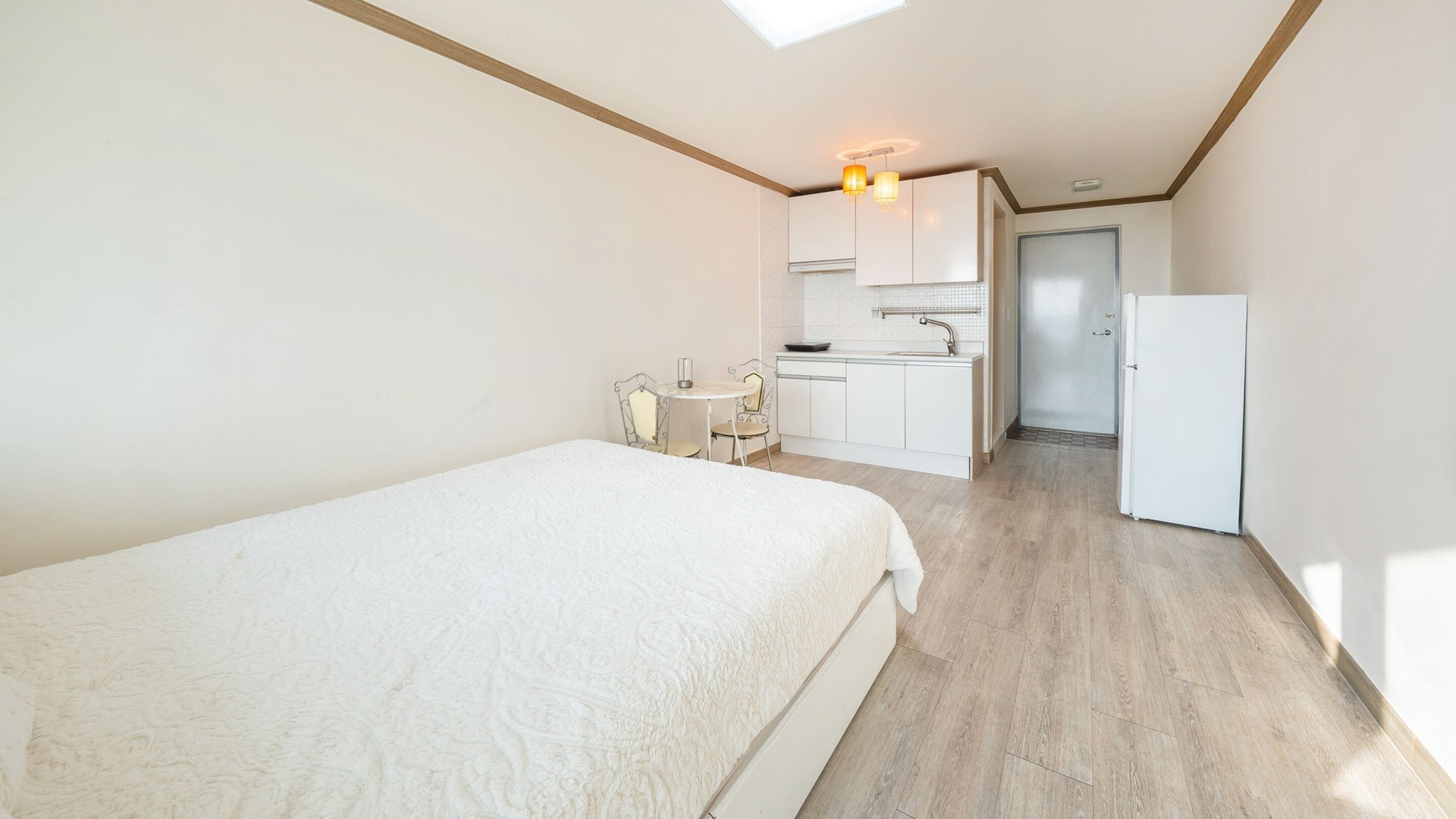A bedroom with a large bed, a small kitchenette with a refrigerator, and a bathroom with a glass shower.