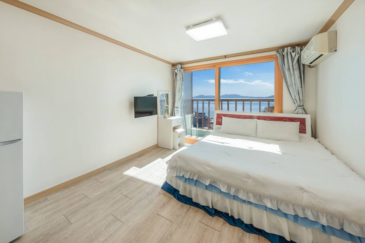A bedroom with a bed, a TV, a window with a view, and a refrigerator.