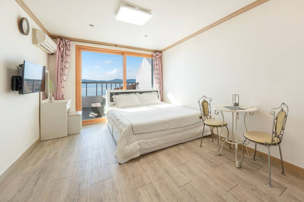 A bedroom with a bed, a small table with chairs, a TV, and a window with a view.
