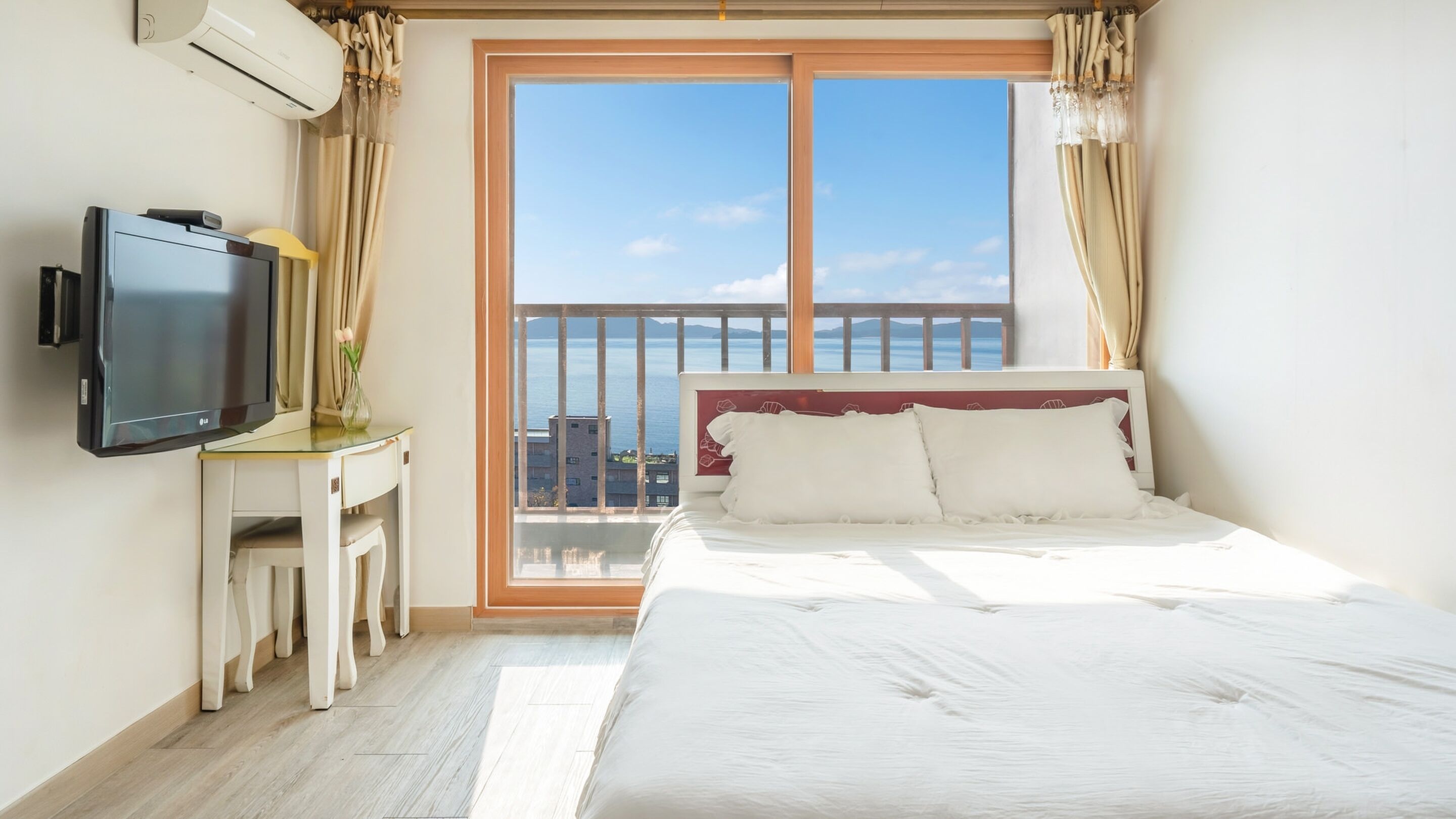 Une chambre d’hôtel équipée d’un lit, d’une télévision, d’un bureau et d’un balcon avec vue sur la mer.