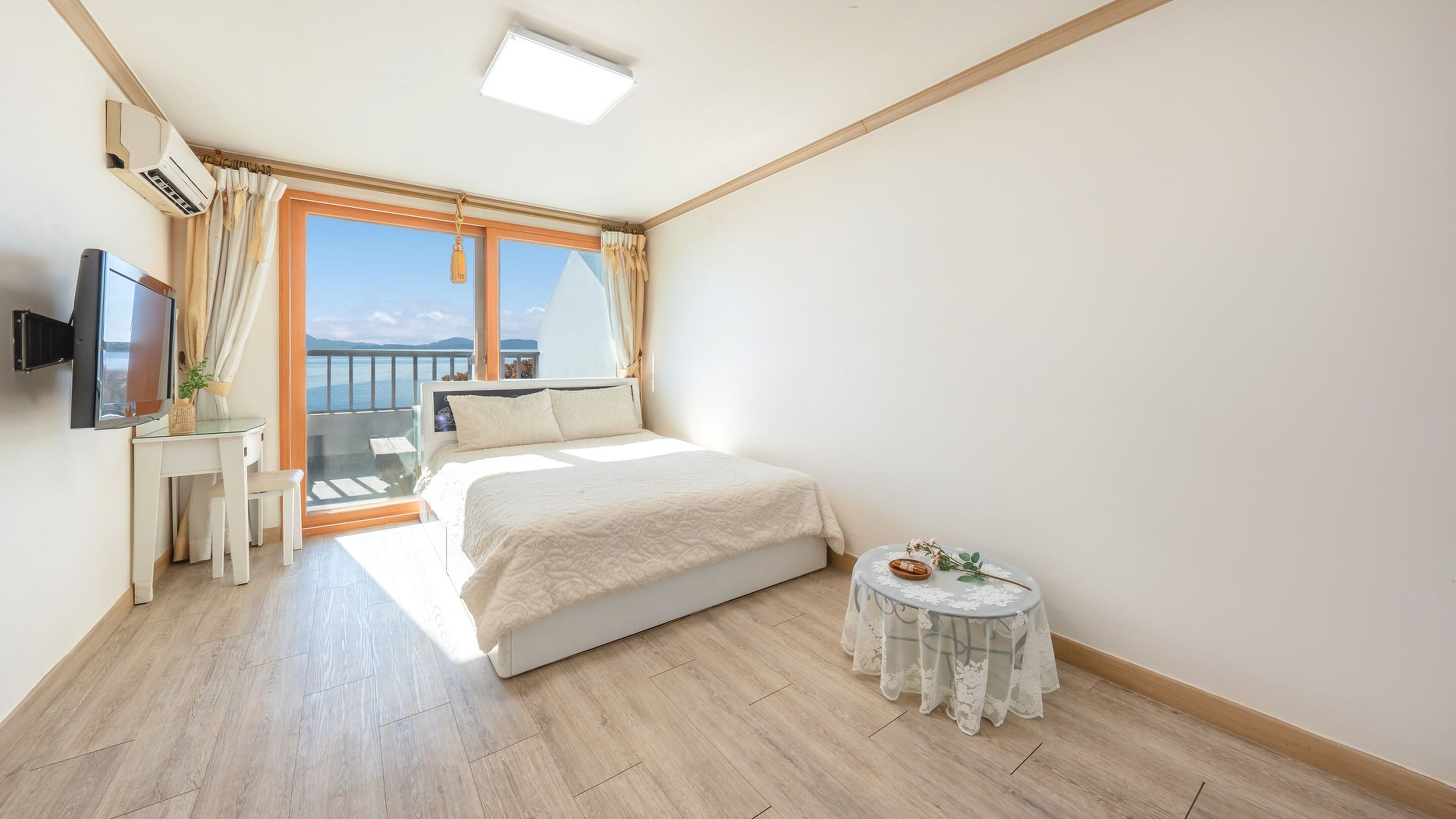 Quarto com cama, televisão, uma mesinha e varanda com vista.