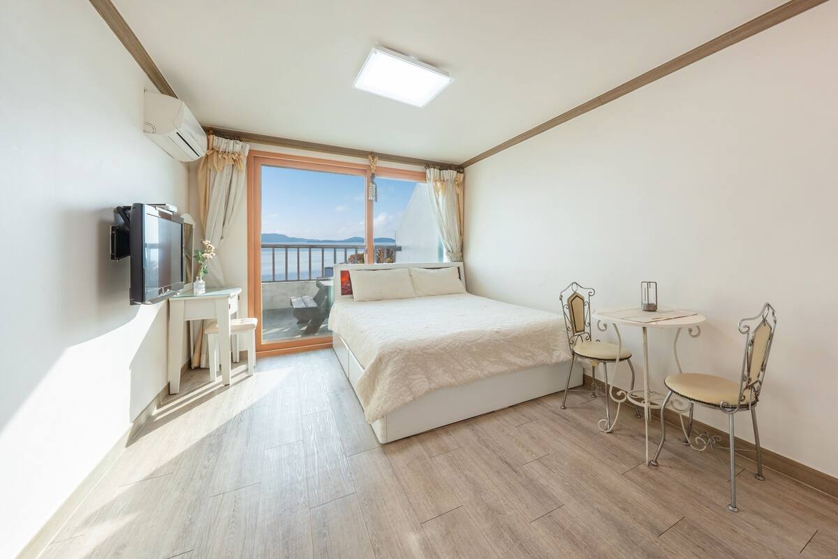 A hotel room with a bed, a TV, a small table with chairs, and a balcony with a view.