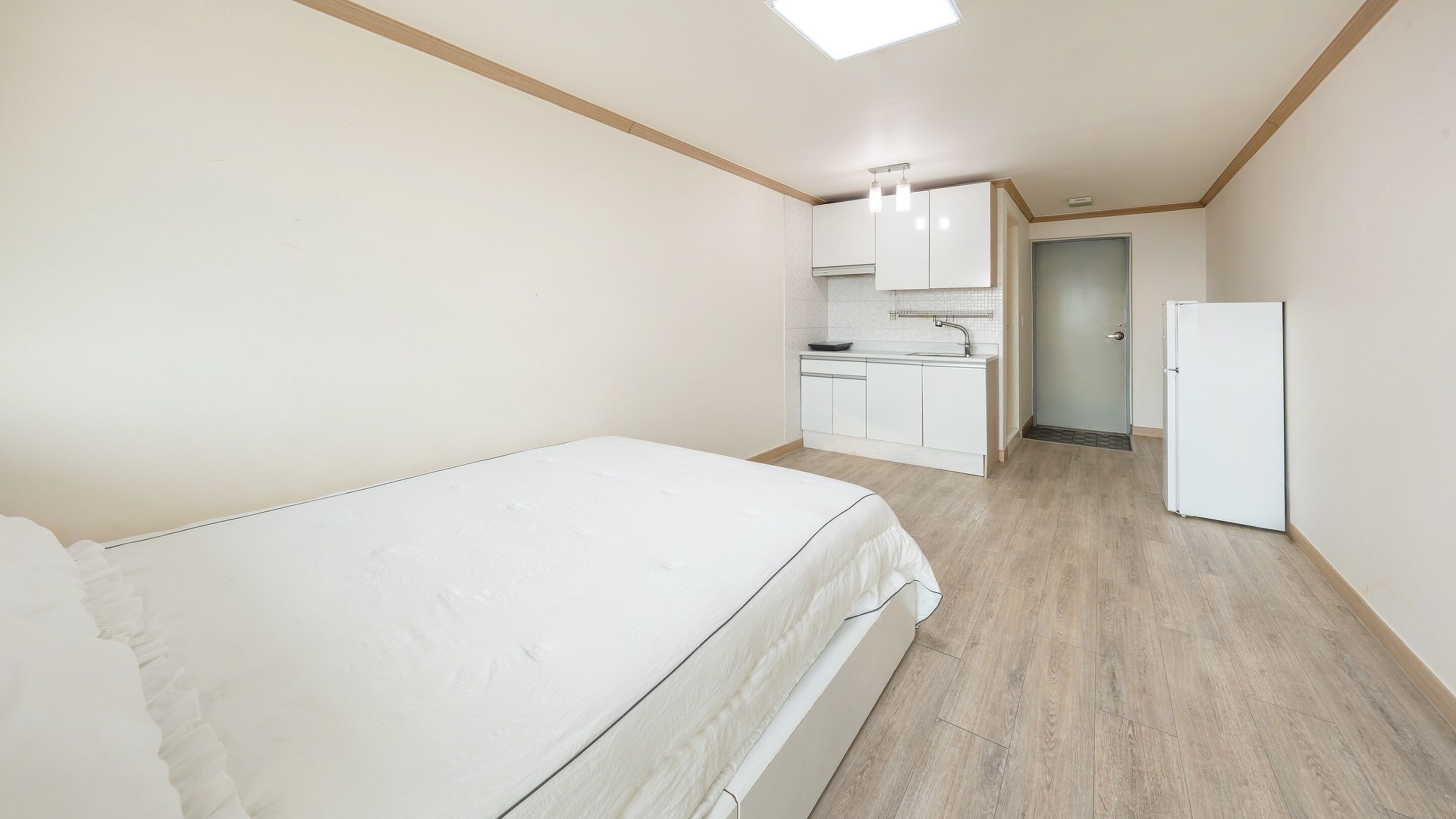 A bedroom with a bed, a kitchenette with a sink and cabinets, and a door leading to another room.