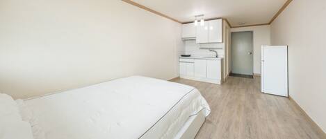 A bedroom with a bed, a kitchenette with a sink and cabinets, and a door leading to another room.