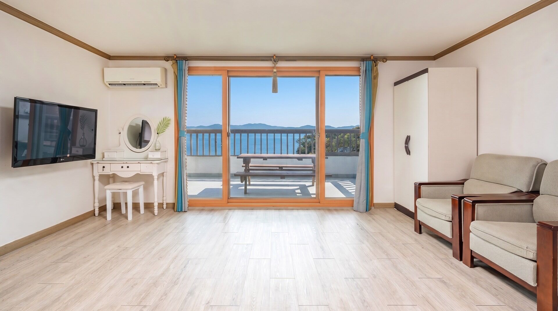 Een kamer met een televisie, een bureau met een spiegel, een stoel, een bank en een balkon met uitzicht.