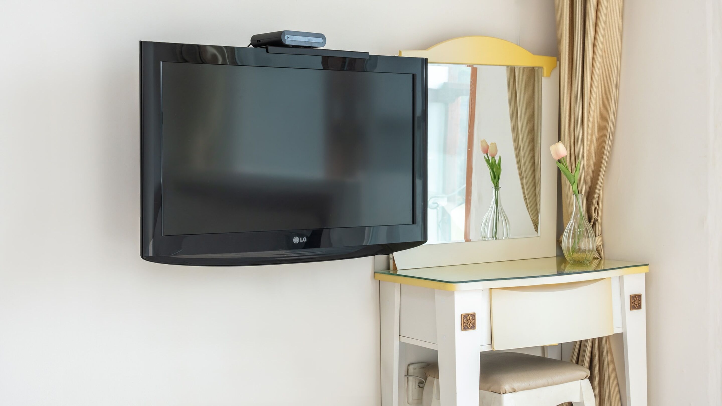 Un televisor de pantalla plana montado en la pared, con una mesa de vidrio debajo.