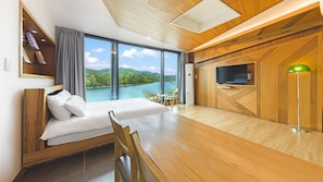 A modern hotel room with a bed, a desk, a TV, and a view of a lake. - Gapyeong Rondavill Pension (Gapyeong)