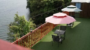 Una terraza con barandilla roja, una mesa y sillas, y dos sombrillas.