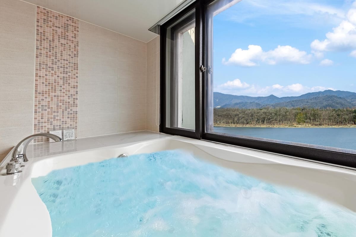 A bathroom with a bathtub, a window, and a view of a lake and mountains.