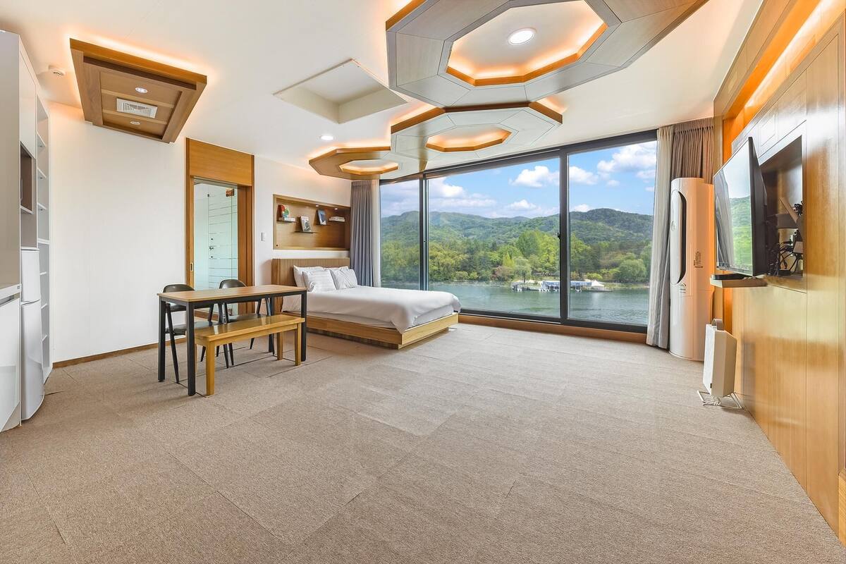 A modern hotel room with a large bed, a dining table, and a kitchen area.