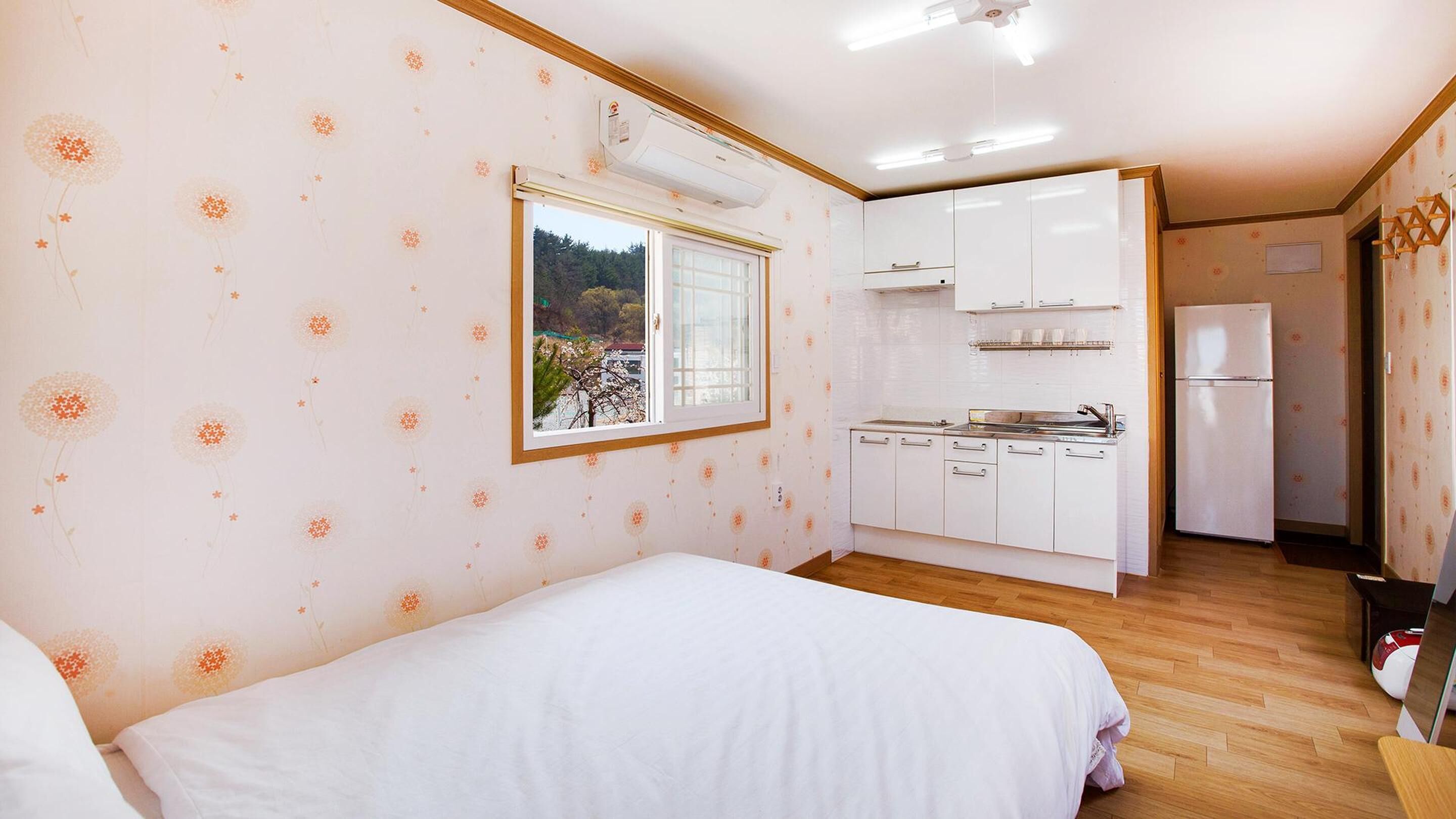 Une chambre comprenant un lit, une fenêtre et une kitchenette équipée de placards et d’un réfrigérateur.