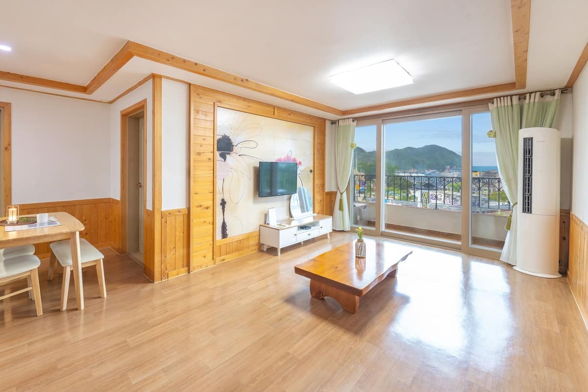 Un vaste espace de vie doté d’un plancher en bois, d’une table à manger avec des chaises, d’un canapé, d’un téléviseur fixé au mur et d’un balcon offrant une vue sur la ville.