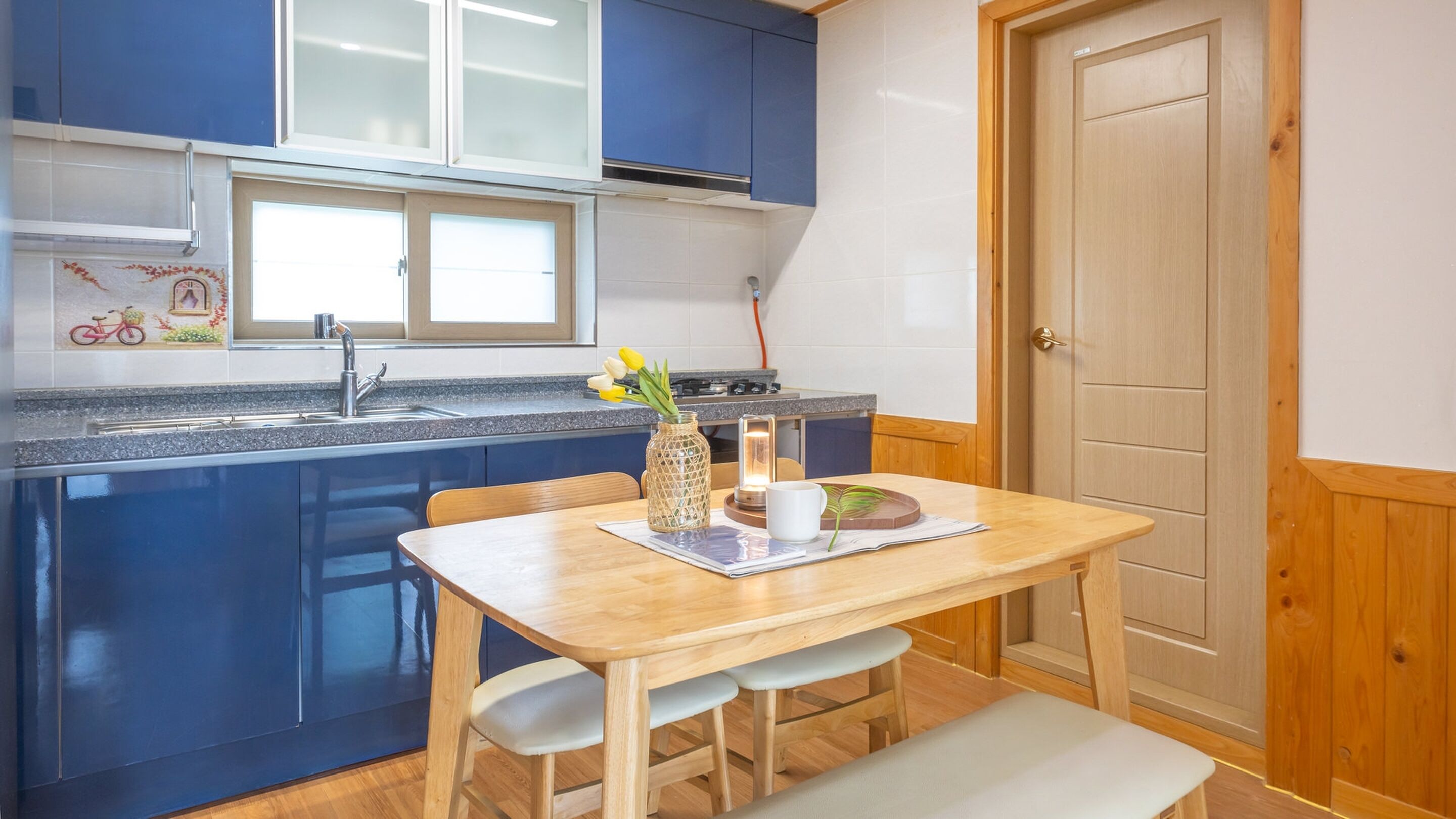 A compact kitchen with blue cabinets, a wooden table, and a bench.