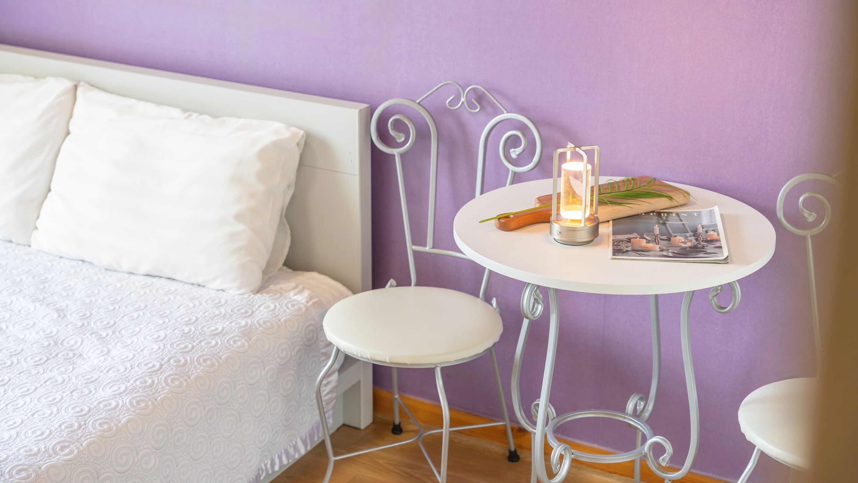 Une chambre à coucher avec un lit, une petite table ronde sur laquelle est posée une bougie, et une chaise.