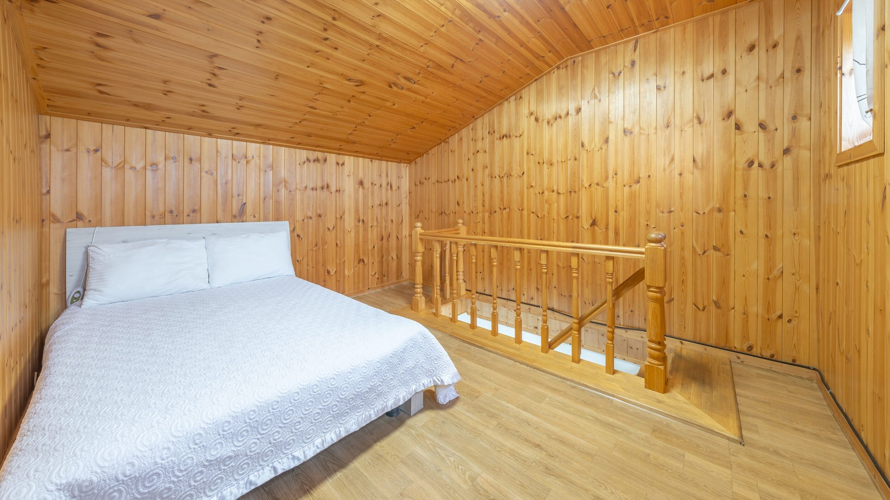 Een slaapkamer met een houten plafond en wanden, een bed met wit beddengoed, en een houten trap.