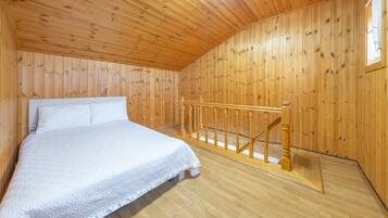 Een slaapkamer met een houten plafond en wanden, een bed met wit beddengoed, en een houten trap.