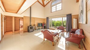 A spacious living room with a fireplace, leather sofas, and a large window offering a view of greenery. - Gapyeong Santa Maria Dog-friendly Privat (Gapyeong)