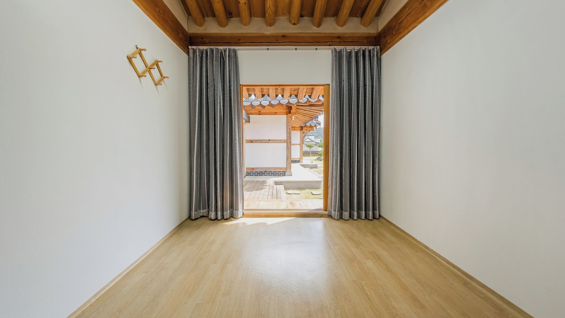 Una stanza con pavimento e soffitto in legno, e vista attraverso una porta con tende decorate.