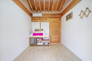 A room with a wooden ceiling, a wardrobe, a shelf with folded blankets, and a small shelf with items.