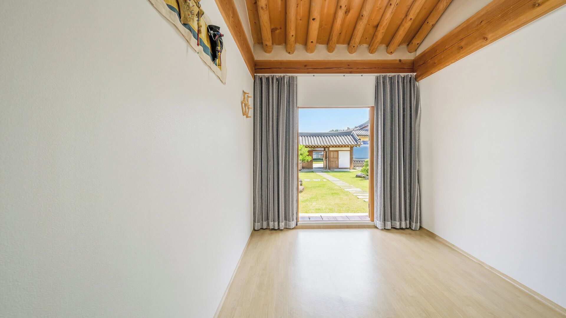 Une pièce avec des poutres en bois, une vue sur un bâtiment traditionnel et une porte coulissante.