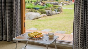Una mesa de desayuno con fruta y un vaso de jugo, una ventana con cortinas y vista a un jardín.