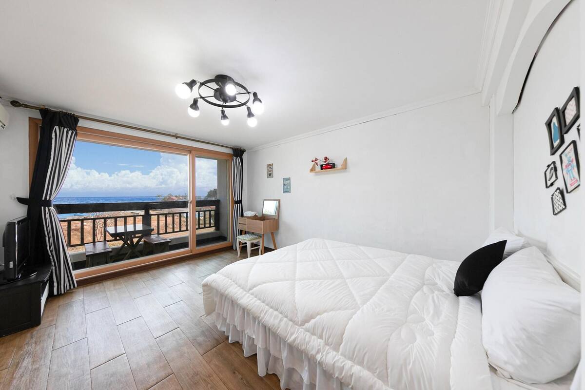 Une chambre dotée d’un grand lit, d’un bureau, d’une chaise, d’une vue sur la mer et d’un balcon avec une balustrade en bois.