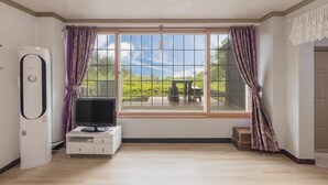 A room with a large window, a flat-screen TV on a white stand, and an air conditioning unit on the wall. - Gangneung Undukmaru Pension (Gangneung)
