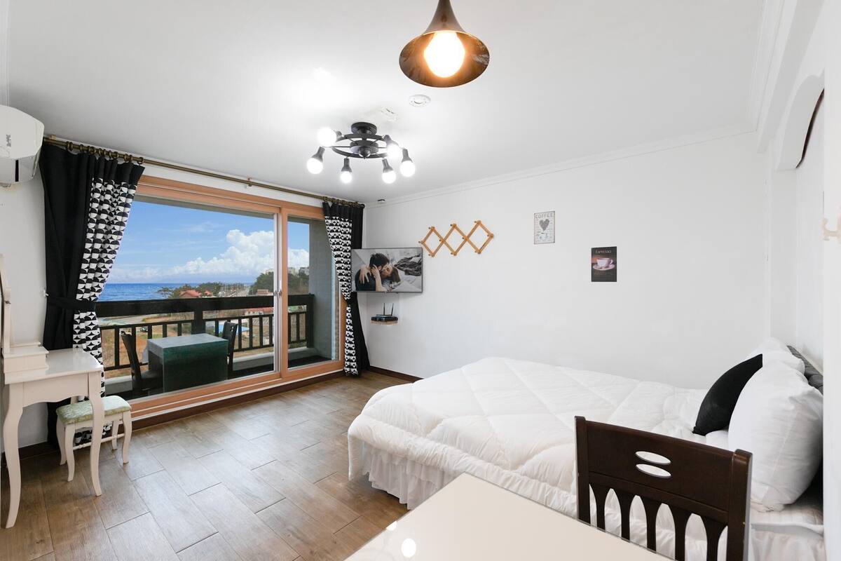 Une chambre avec un lit, un bureau et une chaise, un balcon avec vue et un ventilateur de plafond.