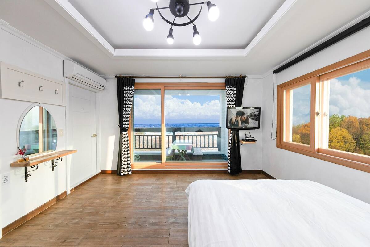 Une chambre à coucher avec un grand lit, un ventilateur de plafond, une télévision et un balcon avec vue sur la mer.
