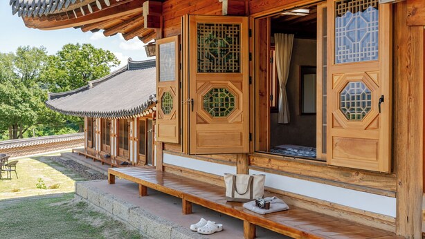 A traditional wooden building with open doors, a bench outside, and a glimpse of a traditional roof.