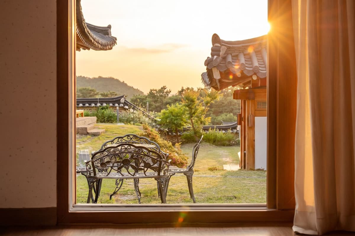A view through a window with traditional architecture, a metal bench, and a curtain.