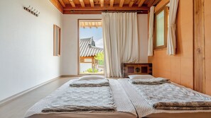 A room with two beds, a wooden ceiling, a window with curtains, and a view of a traditional building outside. - Gyeongju Hanokhotel Chunchugwan (Gyeongju)