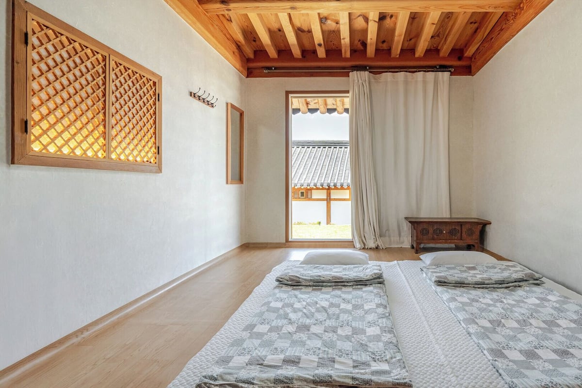 A room with a wooden ceiling, a traditional Japanese sliding door, a bed with patterned bedding, and a small wooden table.