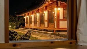 A traditional wooden building with a tiled roof, illuminated by warm lights, and a bench in the foreground.