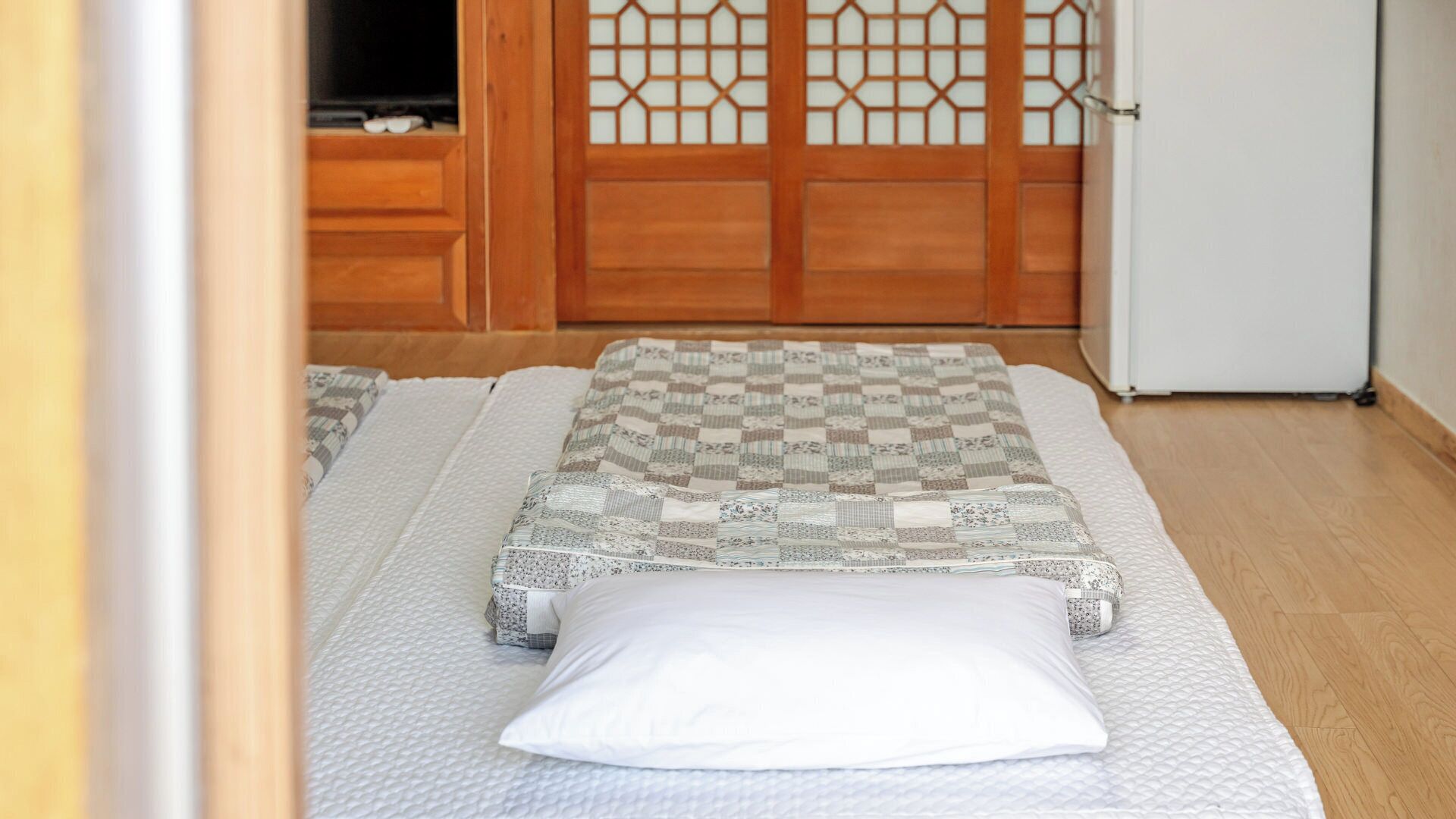 A room with two beds, a wooden door with a lattice design, and a white refrigerator.
