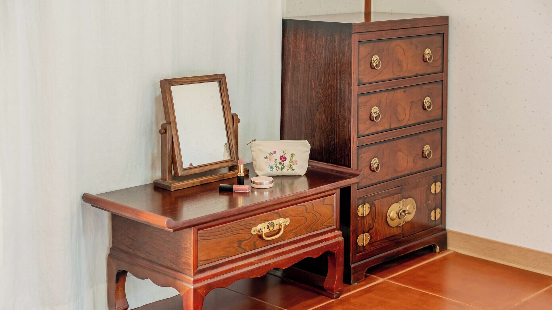 A wooden dresser with drawers and a mirror, a small table with a mirror, and a decorative bag.