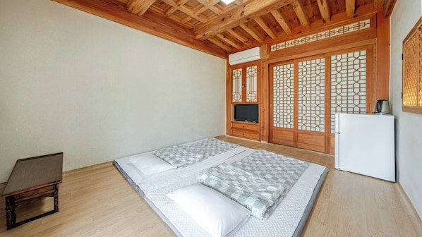 Una habitación con techo de madera, una cama con ropa de cama estampada, una mesita, un televisor y un refrigerador.