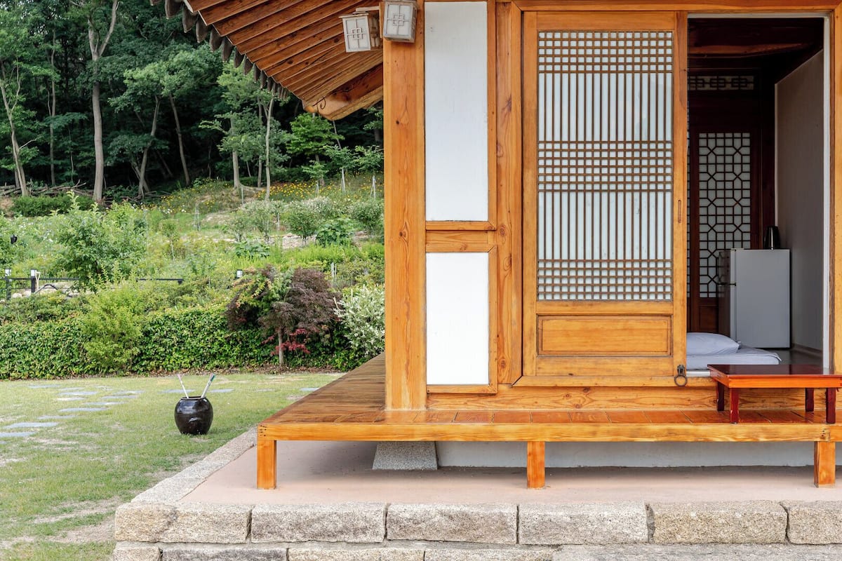 A traditional wooden building with a wooden door, a small bench, and a stone pathway leading to it.