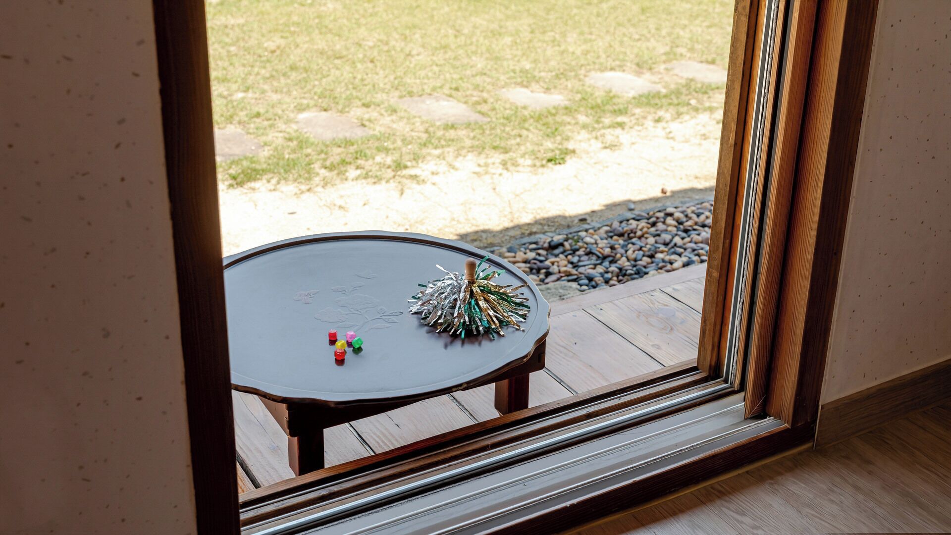 Uitzicht door een raam op een houten terras met een tafel en een potplant.