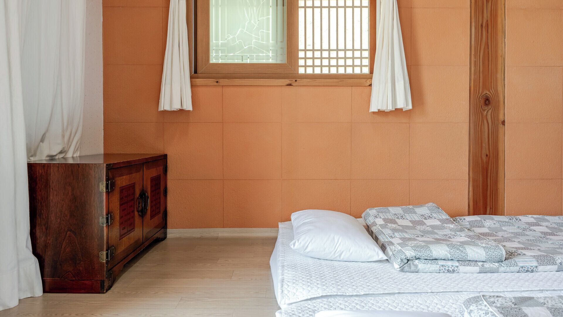 A bedroom with a wooden dresser, a bed with a quilt, and a window with curtains.